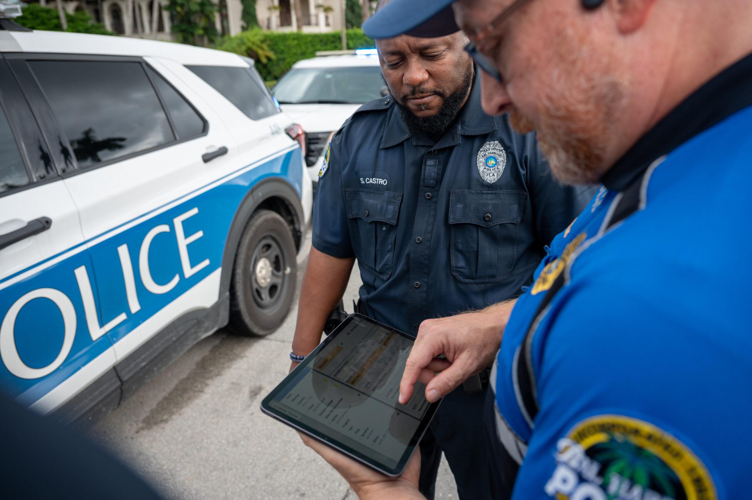two officers standing in front a police car, looking at tablet